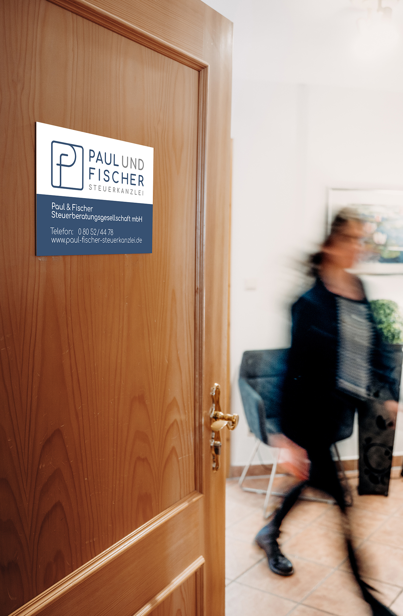 Ein Türschild mit der Aufschrift „Steuerkanzlei Fischer & Paul“ und eine Person geht durch den Raum