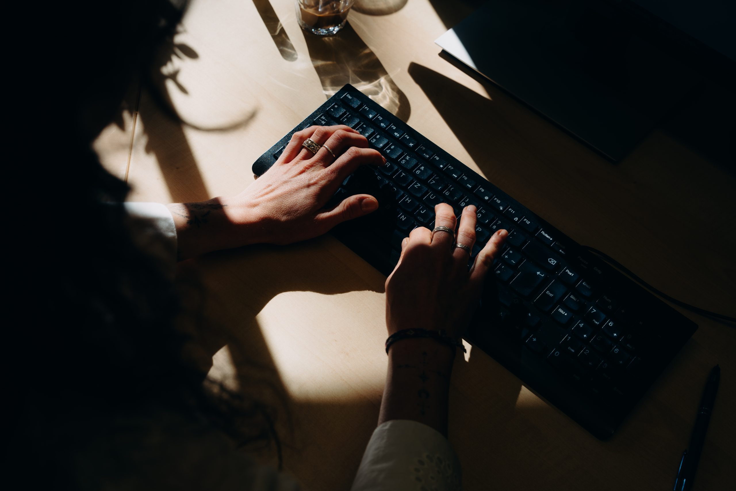 Zwei Hände mit Ringen tippen auf einer schwarzen Computertastatur